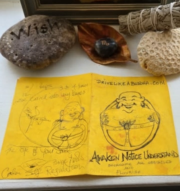 The original Drive Like a Buddha sketch on a folded yellow paper — a Buddha holding a steering wheel, with the words Awaken, Notice, Understand